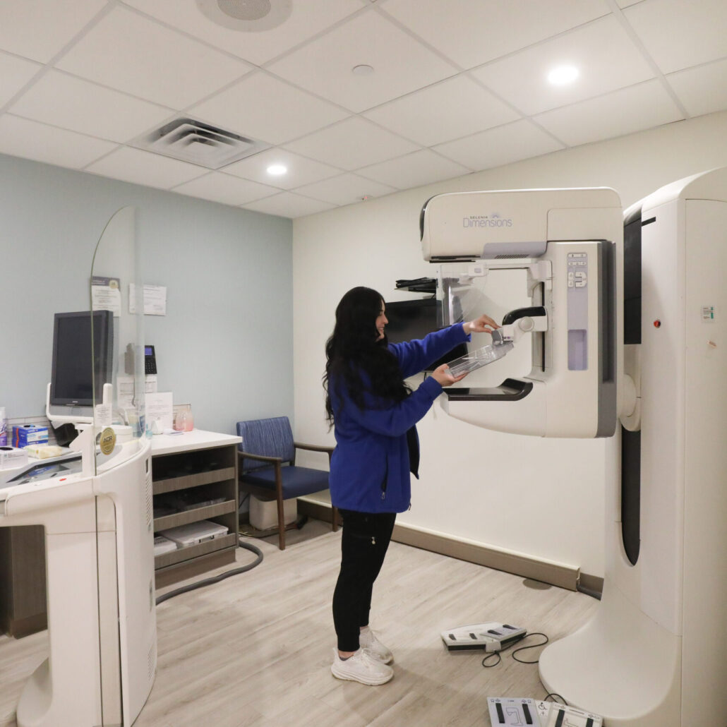 mammography technologist preparing a 3D Hologic Dimensions unit for a breast screening exam in a modern imaging suite