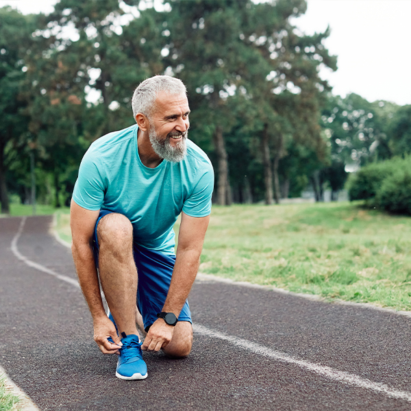 older man in athletic wear ties his running shoes on a track, smiling and ready for a workout