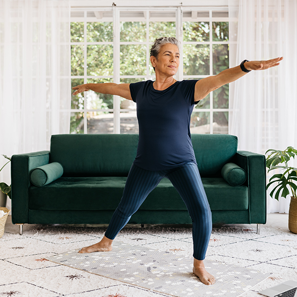 mature woman practices a yoga pose in her living room with natural light streaming through large windows