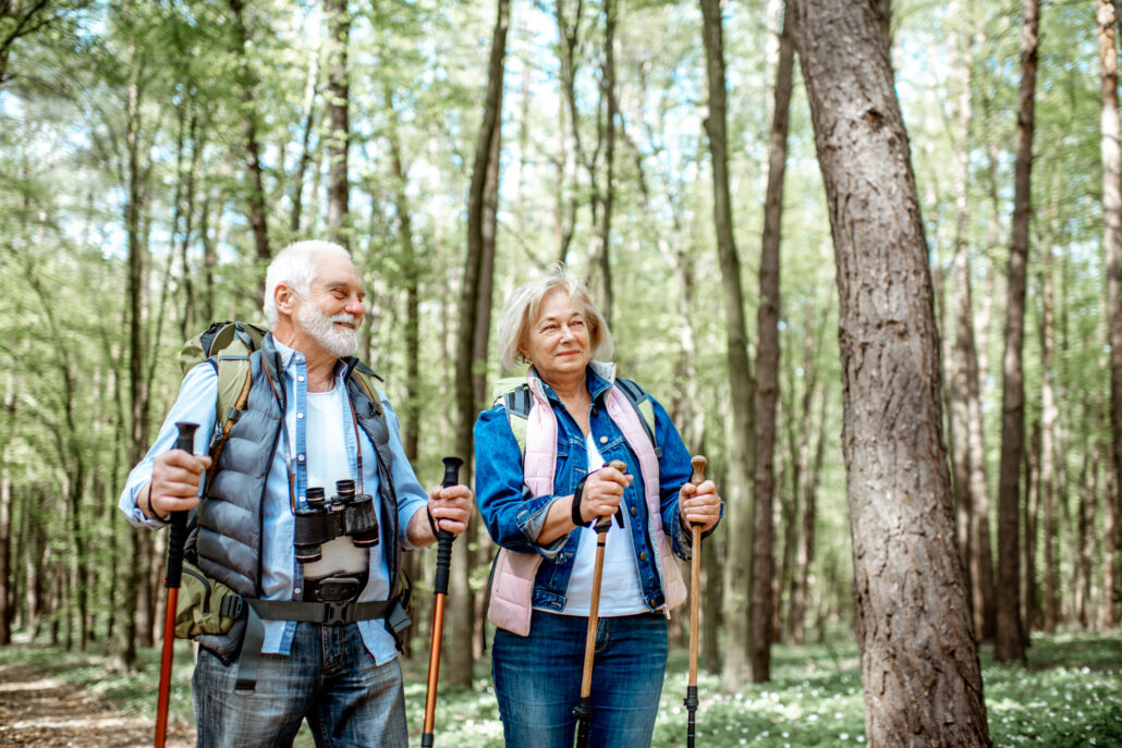 senior couple hiking in the forest equipped with walking sticks and binoculars on a sunny day