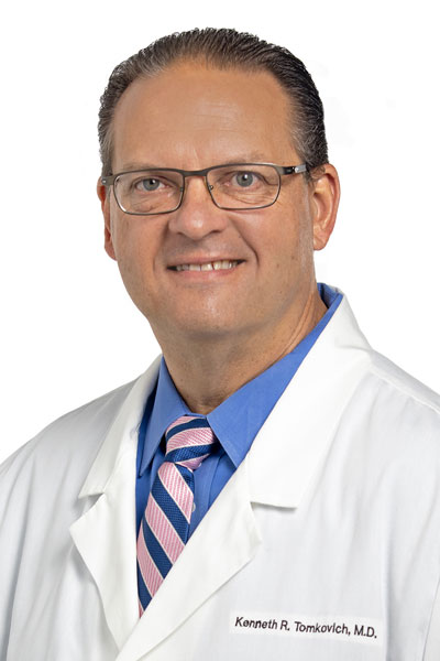princeton radiology doctor in a white lab coat with the name kenneth r tomkovich md stitched on it a blue collared shirt and blue and pink striped tie. the doctor is smiling and wearing glasses