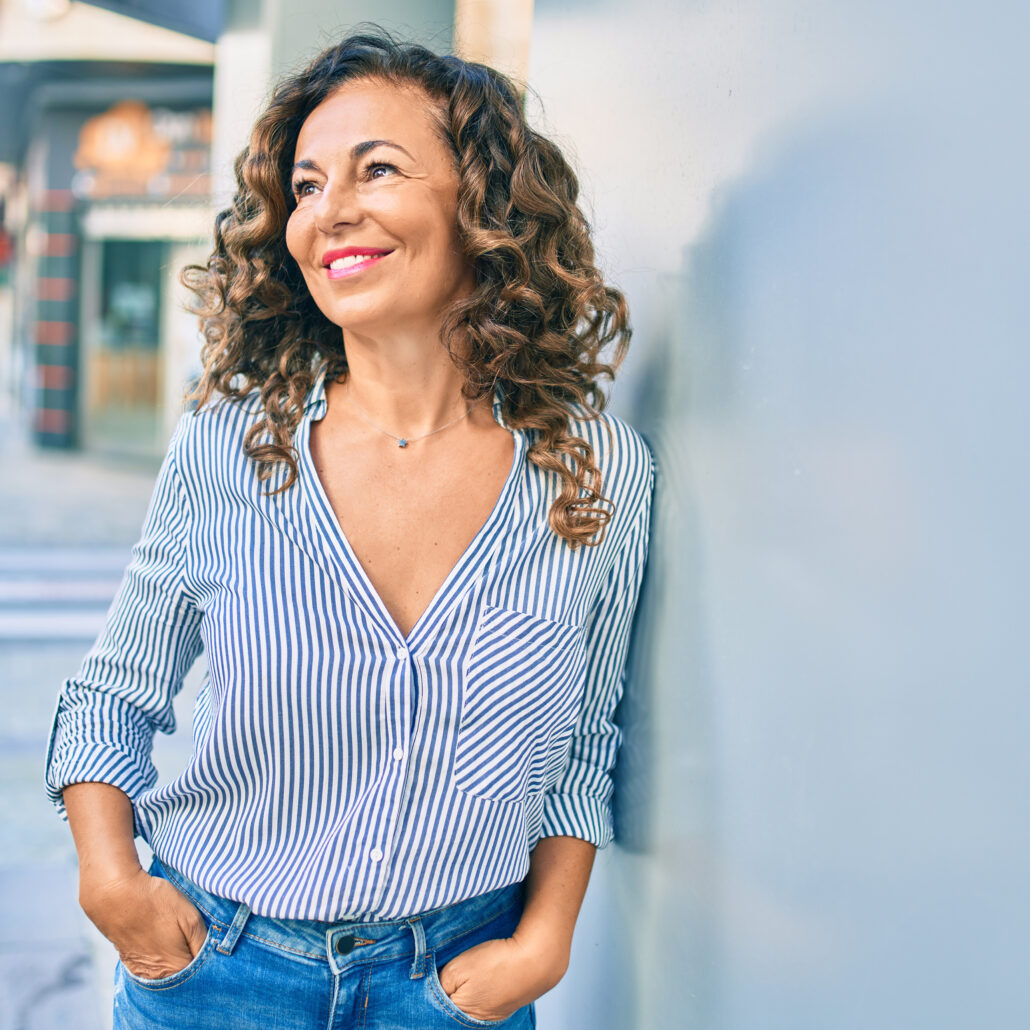 middle age hispanic woman smiling and looking off to the side and leaning against a wall